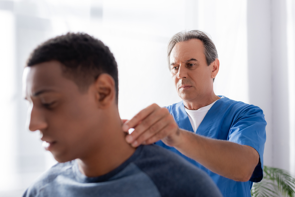 Neck Pain Doctor examining young mans neck
